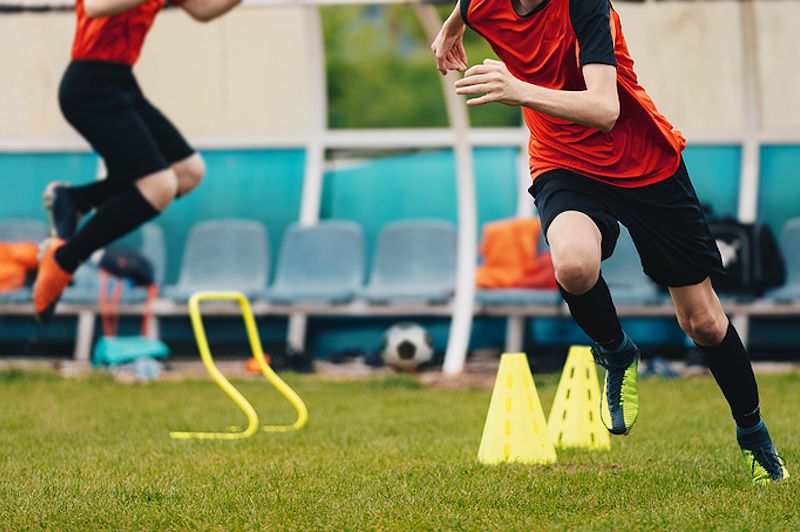 Boys Running Between Cones amd Jumping During Practice in Field on Sunny Day. Young Soccer Players at Speed and Agility Practice Session